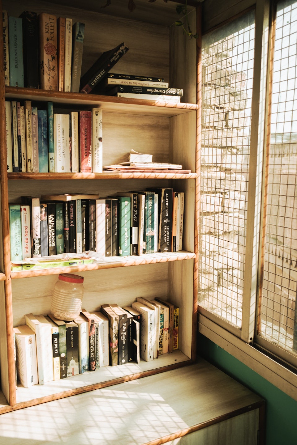 Full wooden bookshelf filled with books and papers near a window.