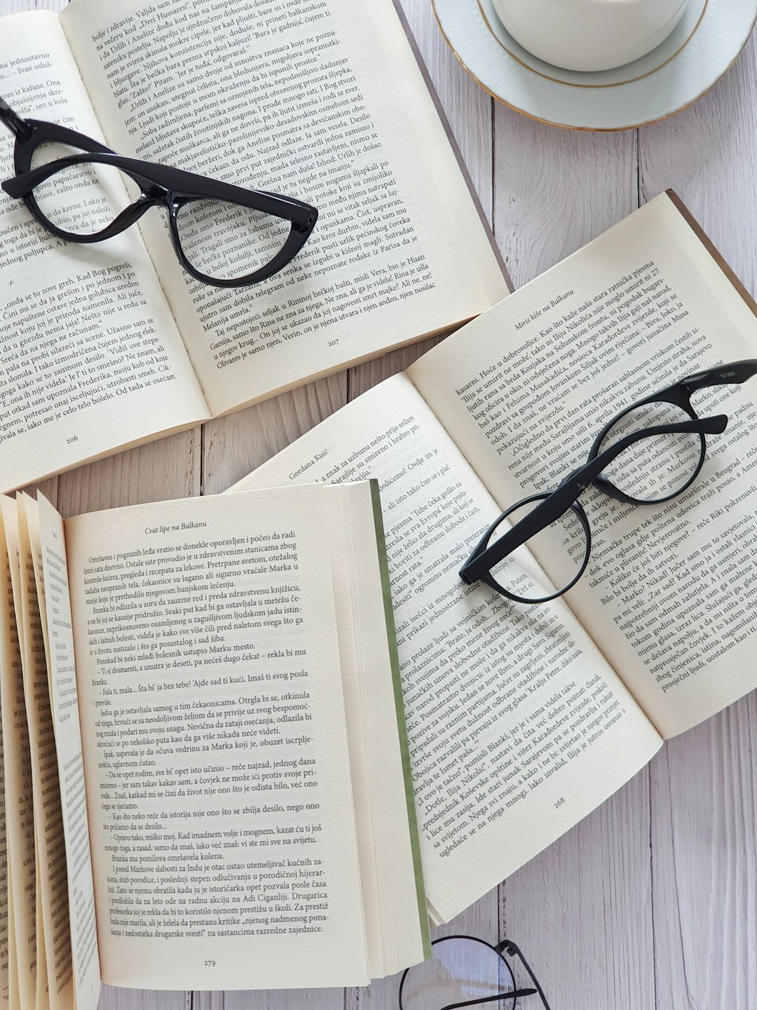 Open books and reading glasses beside a teacup on wood.