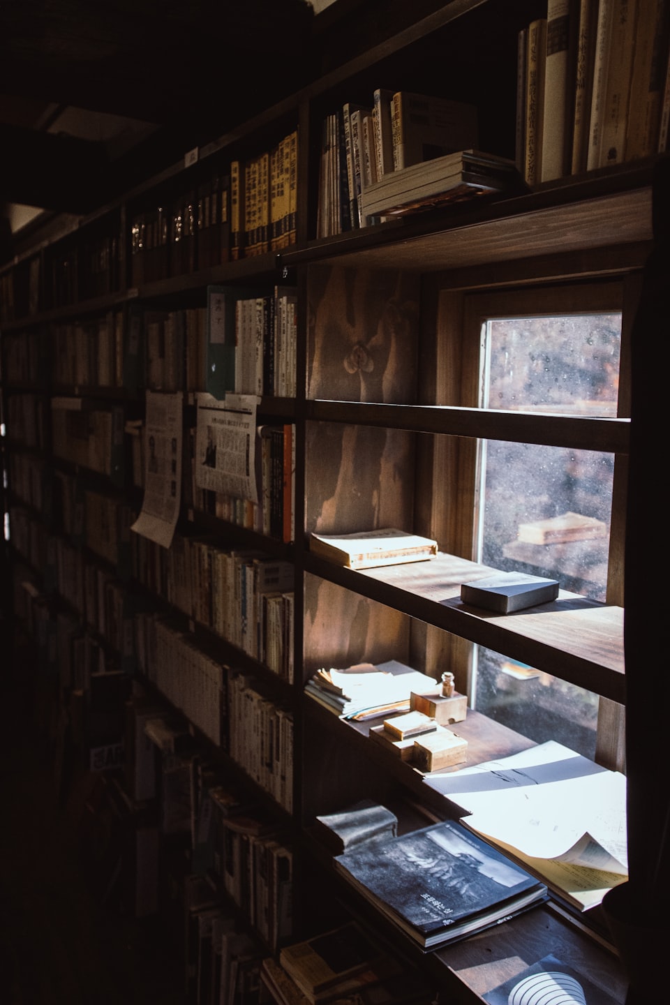 Old wooden bookshelves filled with books near a sunny window.